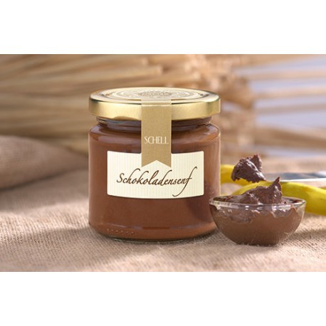 Der Schokoladensenf ist in einem kleinem Glas mit goldenem Deckel, Verschlusssicherung und einem Etikett , daneben steht eine kleine Glasschale mit Schokosenf gefüllt