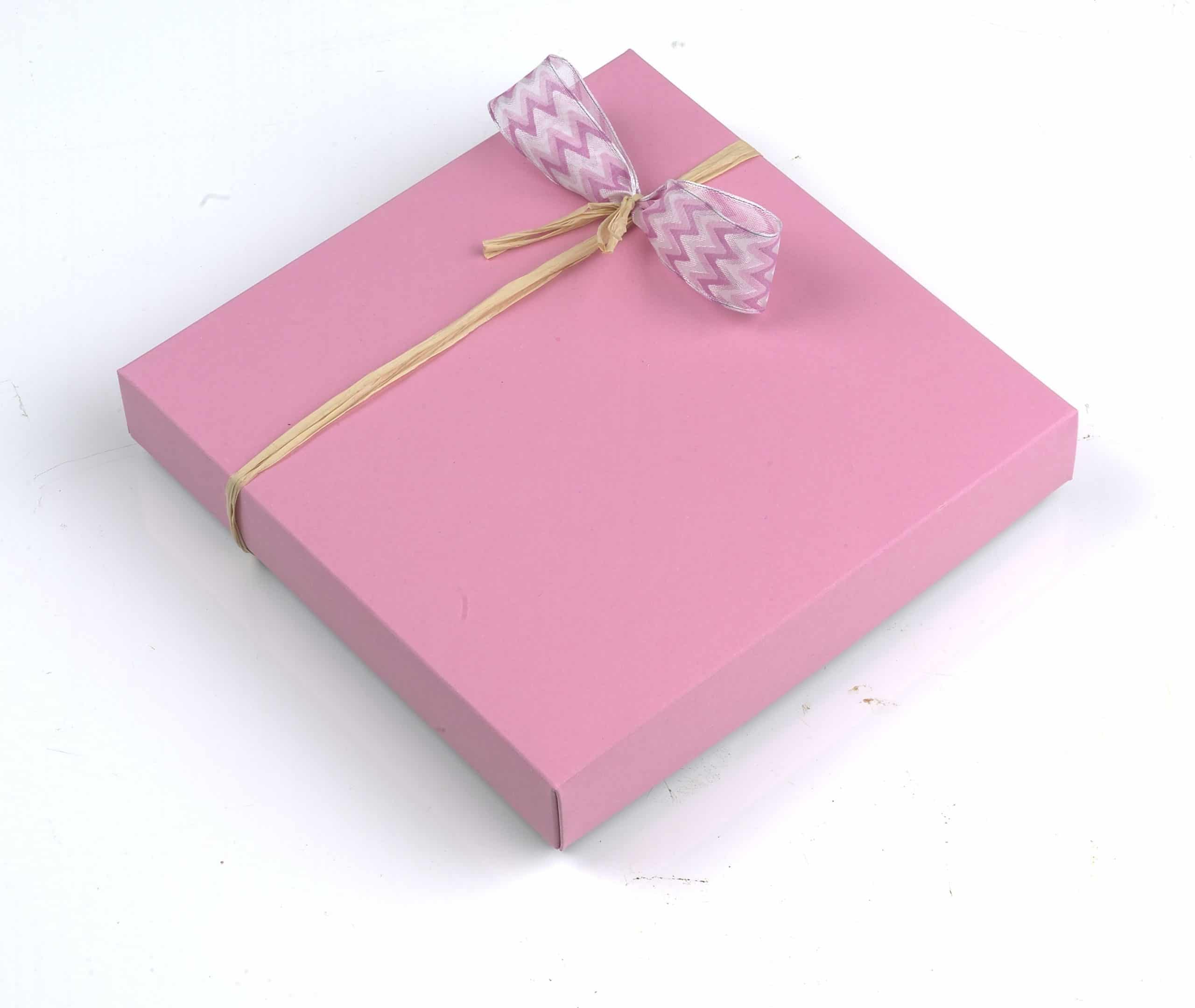16er Schatulle "Rosenzauber" von Schell Schokoladen hat eine pinke Verpackung mit einer pinken Schleife an einem Strohband.