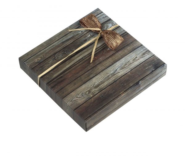 16er Schachtel "Triologie Nougat" . Die Verpackung hat ein hellgraues Holzmuster mit einer braunen kleinen Schleife gebunden.