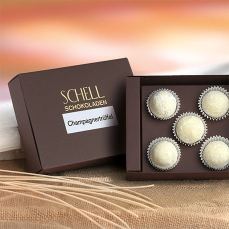 Champagnertrüffel von Schell Schokoladen befinden sich in einer 5er Schachtel mit einer braunen Verpackung, auf dem Deckel steht das Schell Logo und drunter die Pralinensorte.
